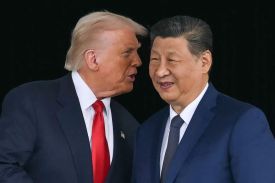 Trump and Xi are seen up close as they stand next to each other, both wearing dark suits and ties and smiling slightly. Trump is leaning closer to whisper something in Xi's ear.