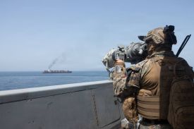 A U.S. service member is seen looking out from a vessel at sea at another vessel.